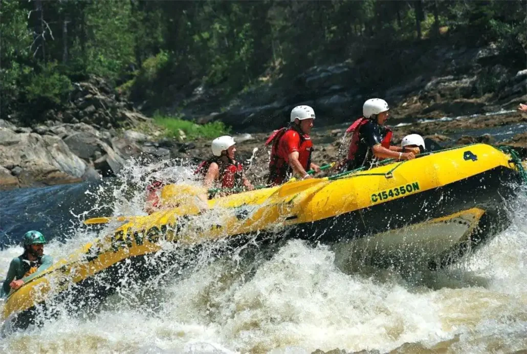 Group of rafters wearing helmets and life jackets paddling a yellow inflatable raft through white-water rapids.